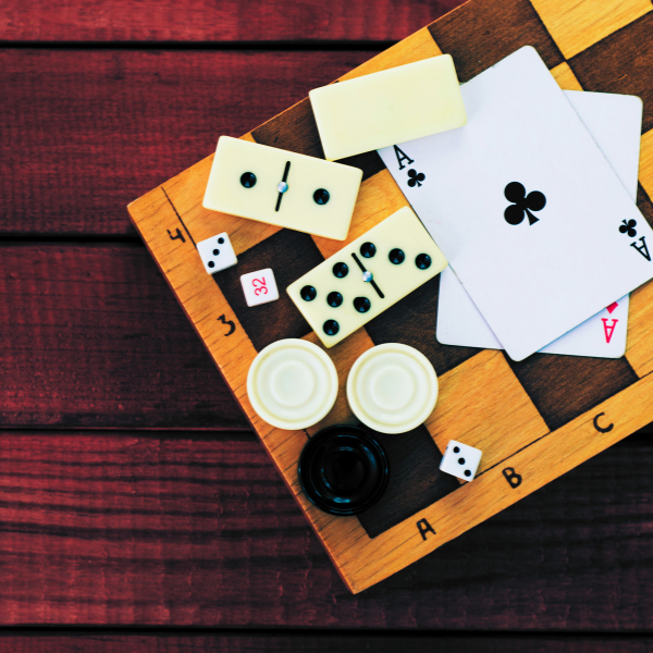 Wooden game board with domino tiles, two white chips, a black disc, dice, and playing cards (Ace of clubs) pictured.