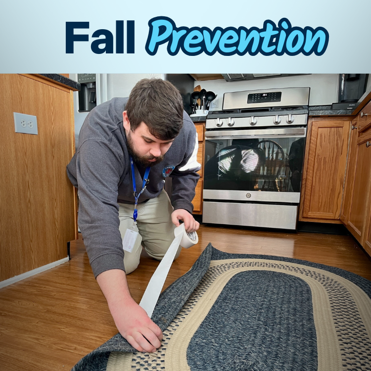 Man applying tape to the edge of a rug in a kitchen to prevent falls, with a Fall Prevention banner above him.